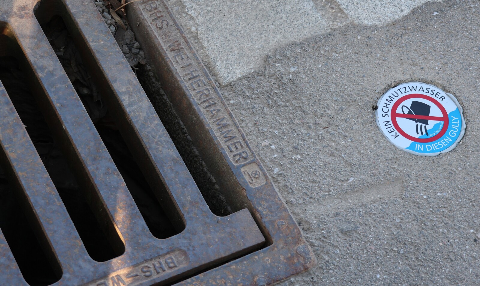 Plakette "Kein Schmutzwasser in diesen Gully" neben einem Gully