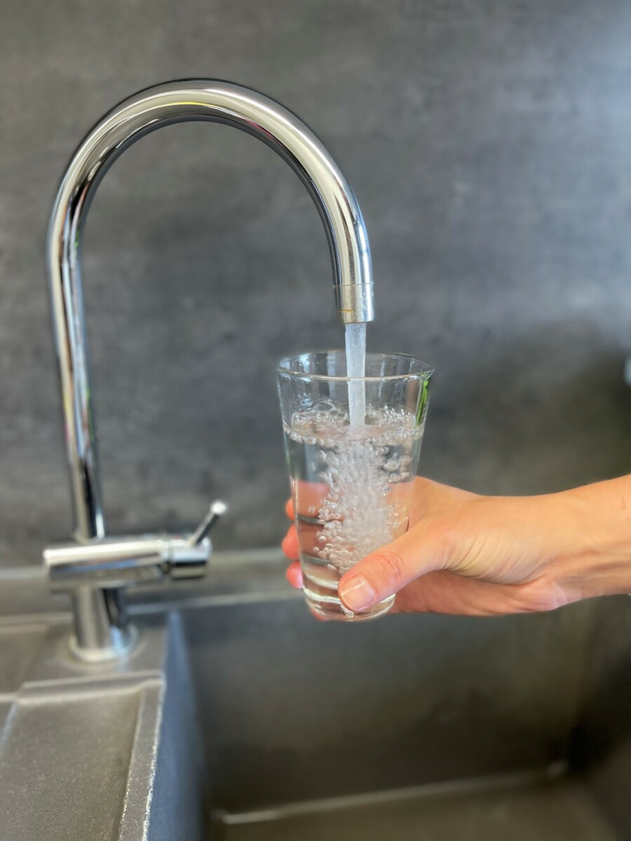trinkwasser Eine Hand hält unter einem offenen Wasserhahn ein Glas und füllt es mit Trinkwasser.